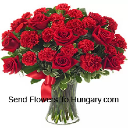 15 roses rouges et 10 oeillets rouges avec quelques fougères dans un vase en verre