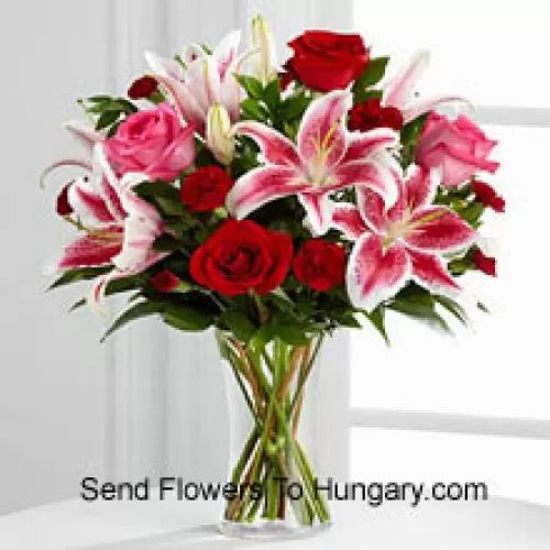 Roses rouges et roses avec des lys roses et des remplisseurs saisonniers dans un vase en verre